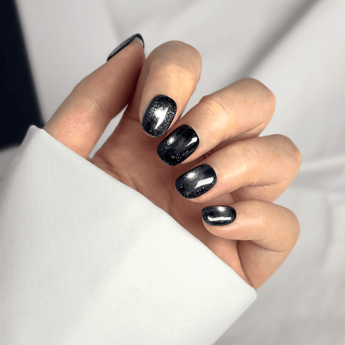 Close-up of a hand wearing MyLilith's black press-on nails with a magnetic cat-eye gel finish, in a short, round shape.