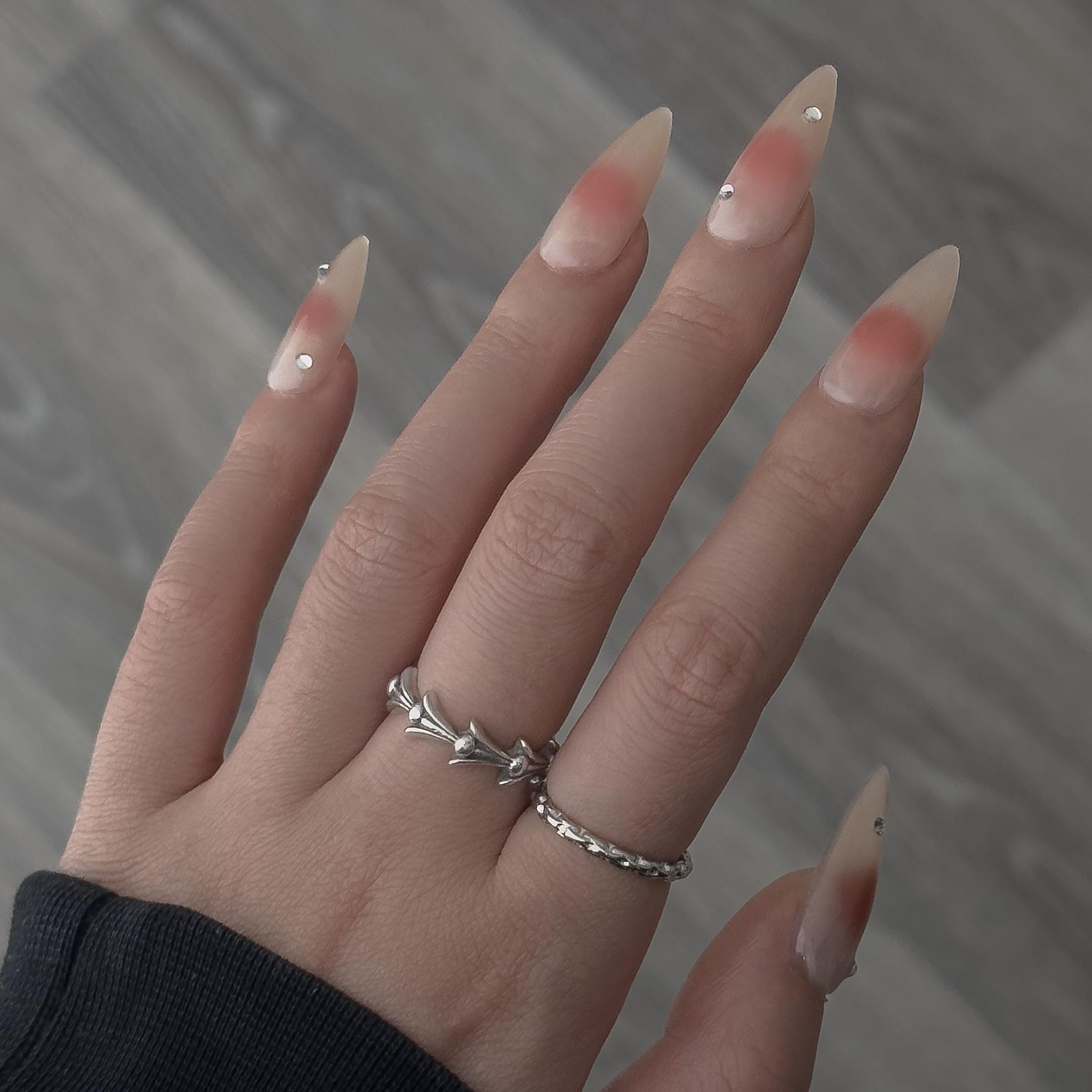 Back-view of a hand wearing MyLilith's press-on nails with a gradient design transitioning from nude to a soft pink at the tips, adorned with small rhinestones, in a stiletto shape.