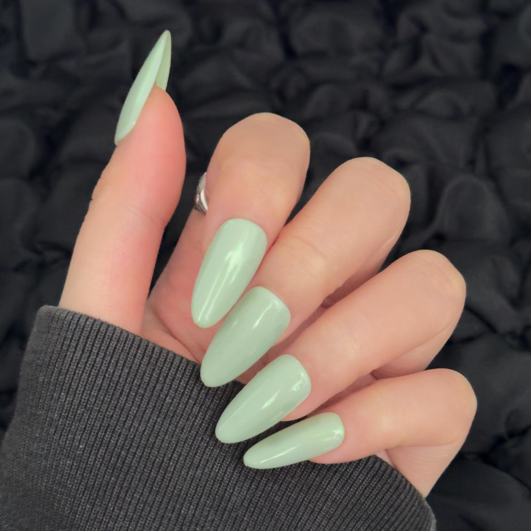 Close-up of a hand wearing MyLilith's mint green press-on nails with a glossy and glazed finish, in an oval shape.