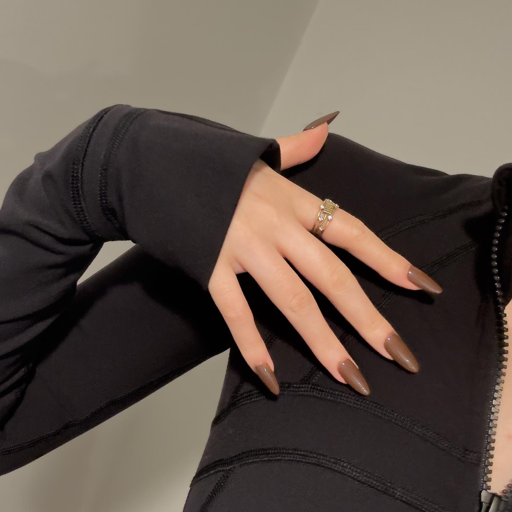 A hand wearing MyLilith's glazed chocolate brown press-on nails with a glossy finish, in an oval shape, on a model wearing a black long-sleeve top.