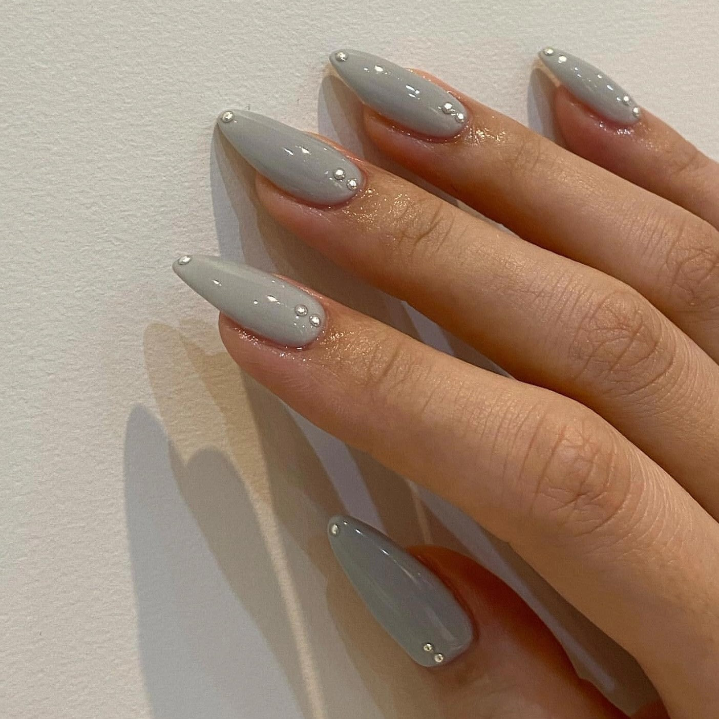 Close-up of a hand wearing MyLilith's grey press-on nails with a glossy finish, adorned with small rhinestone accents, in an almond shape.