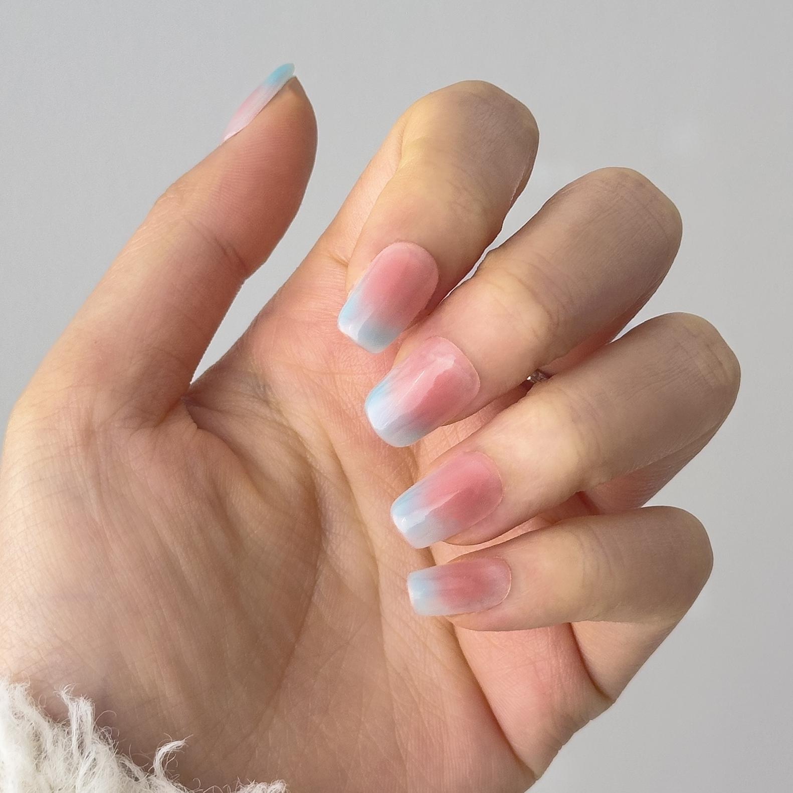Close-up of a hand wearing MyLilith's press-on nails with a pastel ombre design, transitioning from pink at the base to blue at the tips, in a medium, coffin shape.