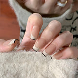 Close-up of a hand wearing MyLilith's modern French tip press-on nails with a glossy finish, featuring black tips and a nude base, in a short, coffin shape.