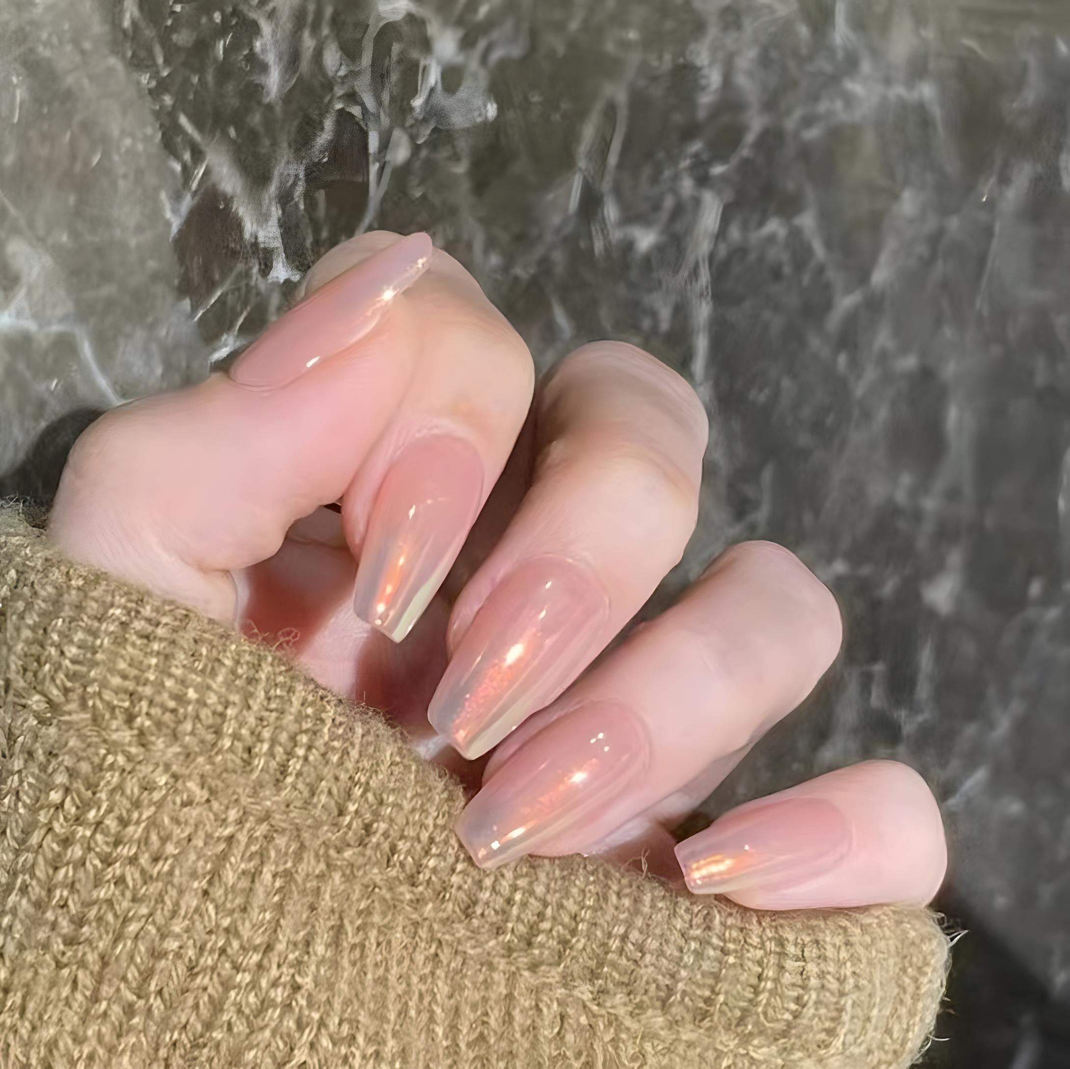 Close-up of a hand wearing MyLilith's iridescent nude press-on nails with a glossy finish, giving orange sunset hues, in a short coffin shape