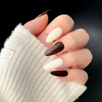 Close-up of a hand wearing MyLilith's chocolate brown and cream white press-on nails with an almond shape.