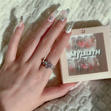 Back-view of a hand wearing MyLilith's handmade press-on nails featuring various designs, including chrome accents, a pink 3D heart, pearl embellishments, and silver studs, in a medium-length, coffin shape.