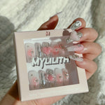 Close-up of a hand wearing MyLilith's handmade press-on nails featuring various designs, including chrome accents, a pink 3D heart, pearl embellishments, and silver studs, in a medium-length, coffin shape.