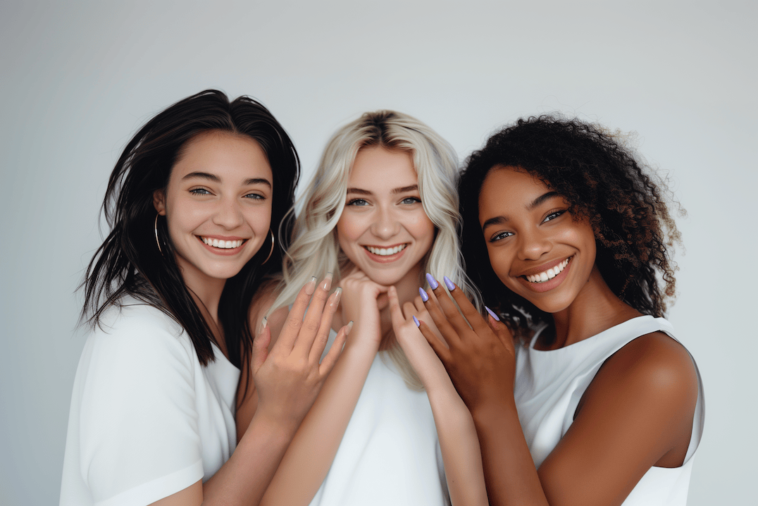 Three smiling women of diverse backgrounds showcasing their MyLilith press-on nails, standing close together in white outfits.