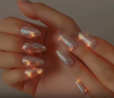 Video of two hands wearing MyLilith's press-on nails with a shiny, pearl-like finish and adorned with small shining rhinestones, in an almond shape.