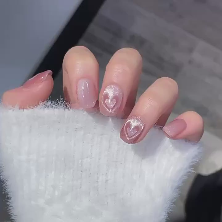 Video of a hand wearing MyLilith's pink cat-eye magnetic press-on nails with a glossy finish, featuring an accent nail with a heart design, in a short, squoval shape. The heart accent appears to beat as the wearer's fingers move.